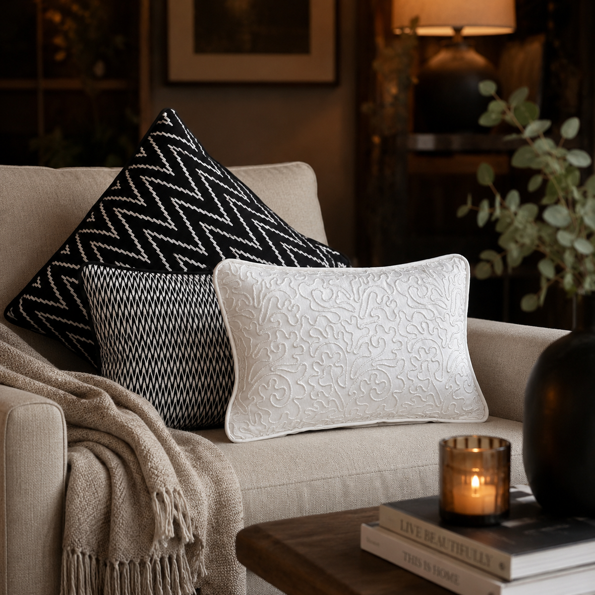 Black and white designer cushion cover set styled on a beige sofa in a luxury living room, featuring geometric patterns and elegant embroidered detailing for modern home décor by Inara Home Decor.