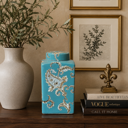 Elegant blue ceramic decorative jar styled with artwork, books and olive branches on a luxury console table for sophisticated interior décor.