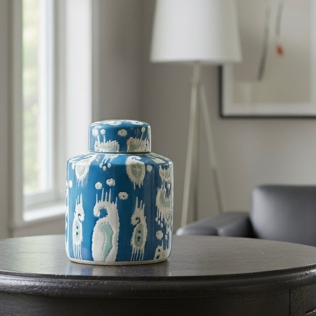 A handcrafted blue and white ikat ceramic ginger jar with a matching lid, styled on a dark wood side table in a bright, modern living room with soft natural lighting.