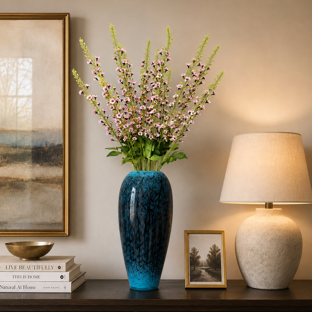 Blue marbled ceramic floor vase with delicate pink flowering stems displayed on a dark wood console table against a neutral wall in an elegant modern living room.