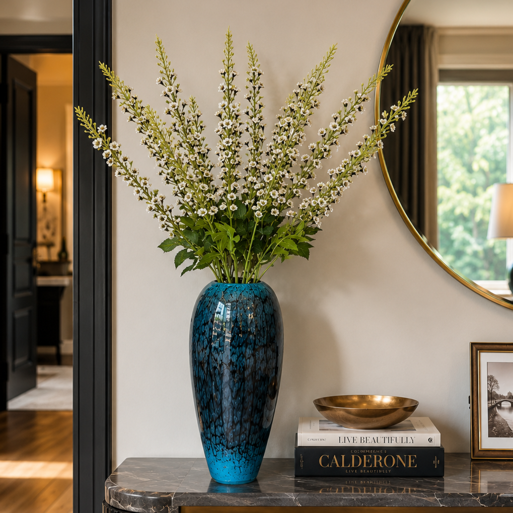 Elegant blue decorative vase with white floral stems displayed on a luxury black console table with gold accents, styled in a modern entryway featuring a round mirror and sophisticated home décor.