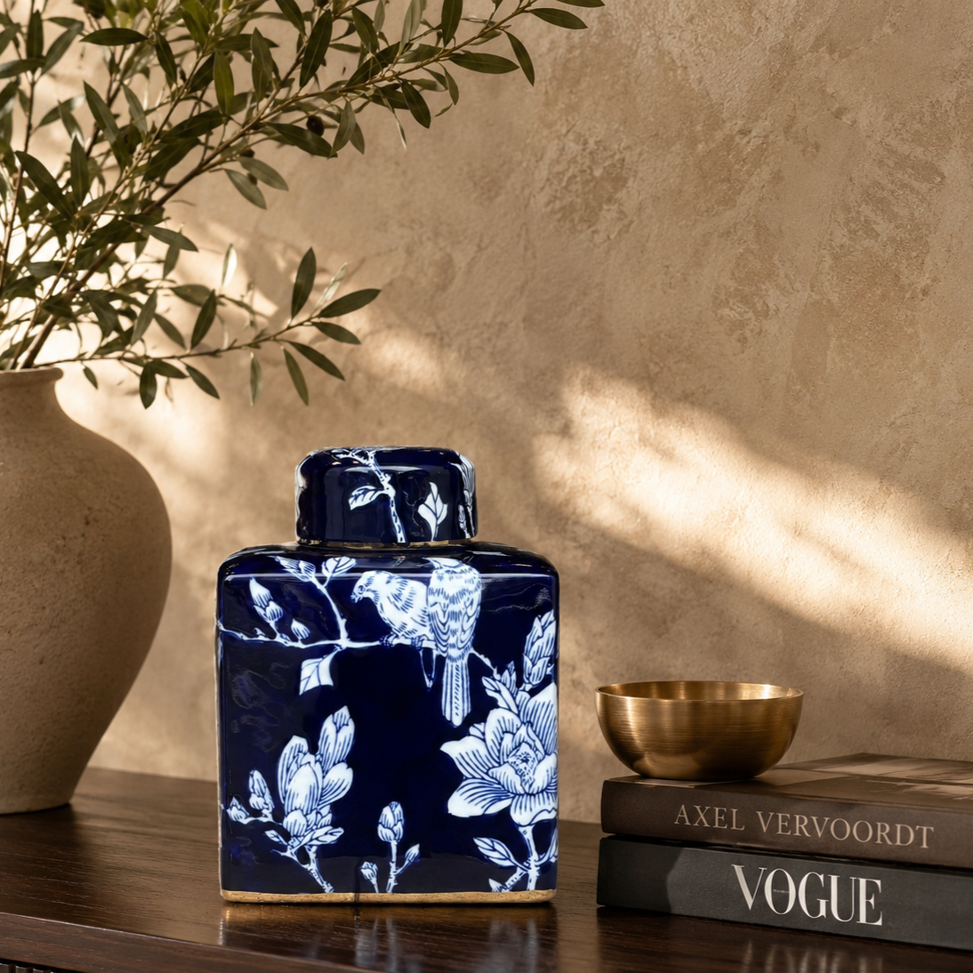 Hand-painted blue and white ceramic ginger jar styled on a luxury wooden console table with olive branches and designer books.