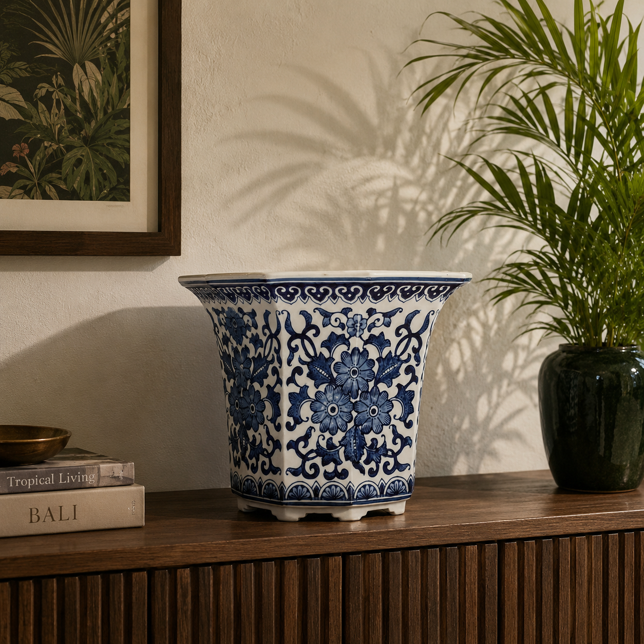 Blue and white floral ceramic planter styled on a wooden console table against a textured wall with tropical decor accents and warm natural lighting.
