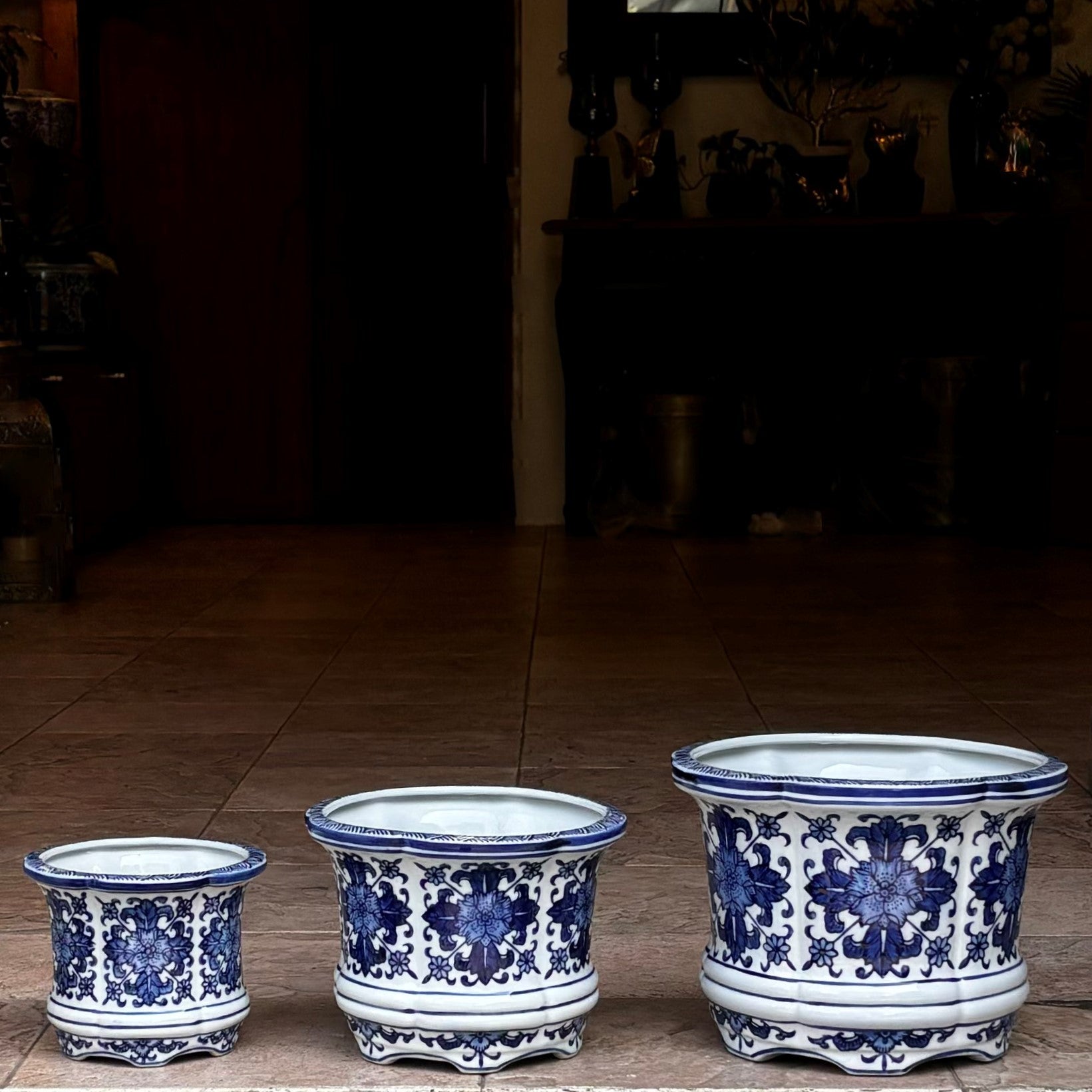 Set of three blue and white hand-painted ceramic floral planters in different sizes displayed on a tabletop, showcasing intricate traditional patterns.