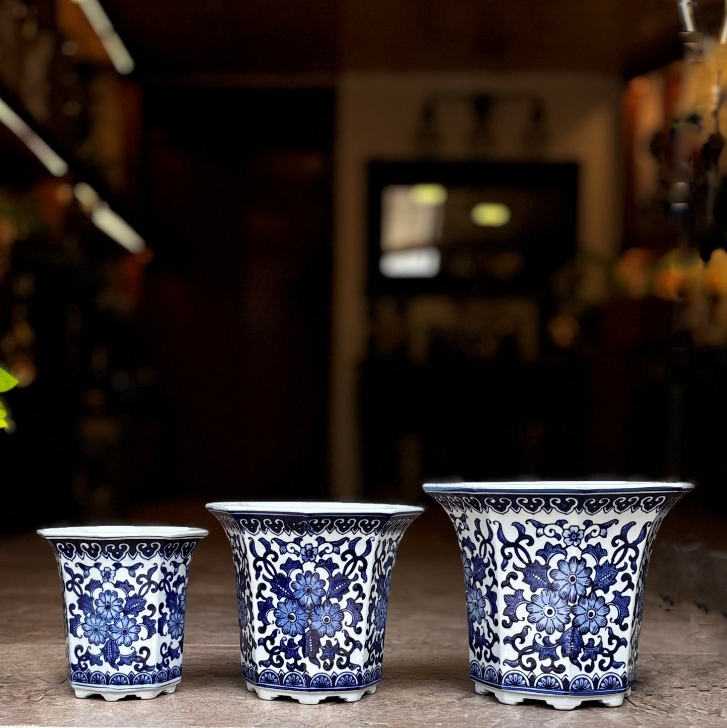 Set of three blue and white hand-painted ceramic planters with floral motifs displayed on a tabletop.