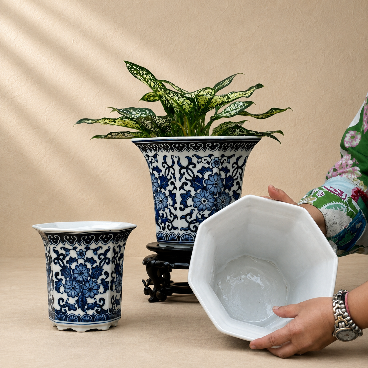 Blue and white porcelain planter showing the spacious glazed interior while held by hand for size reference alongside a planted decorative pot.