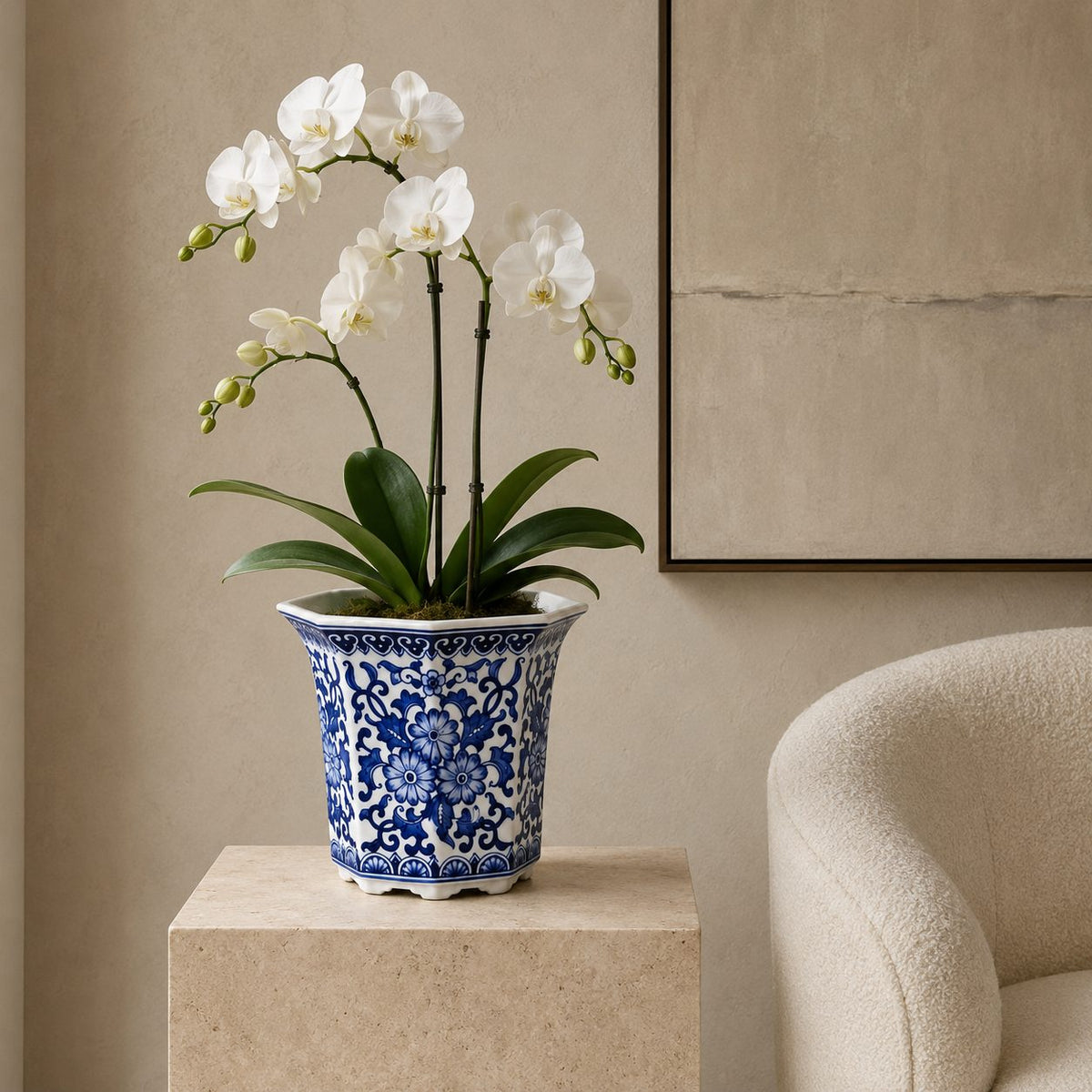 Blue and white floral porcelain planter styled with a white orchid on a stone pedestal in a modern luxury living room.