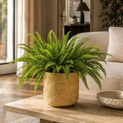 Lush Boston fern in a gold textured leaf-pattern ceramic planter on a travertine coffee table in a neutral, cozy living room