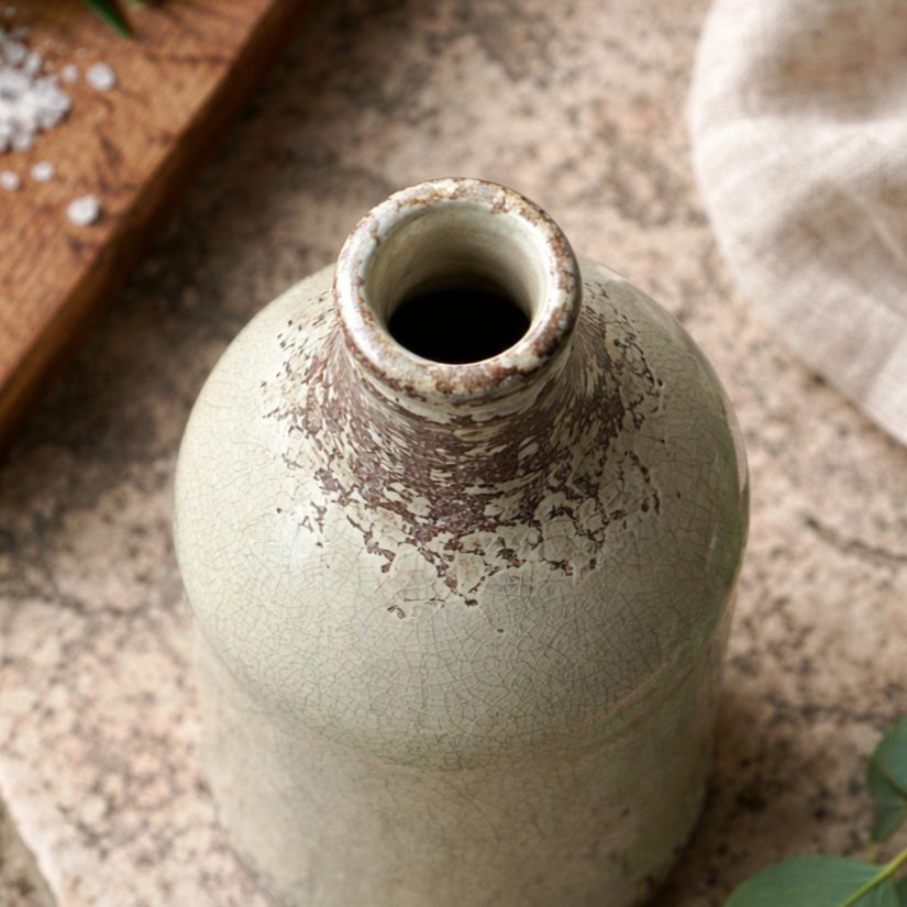 Top view lifestyle image of a rustic crackle glaze ceramic vase with distressed brown detailing on a textured stone surface, styled with eucalyptus leaves in natural light.