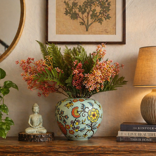 Ceramic floral vase with artificial flowers styled on wooden console table with Buddha statue, lamp, and home decor accents