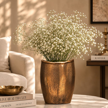 Antique bronze handcrafted metal vase styled with baby's breath flowers on a marble coffee table in a luxury living room.