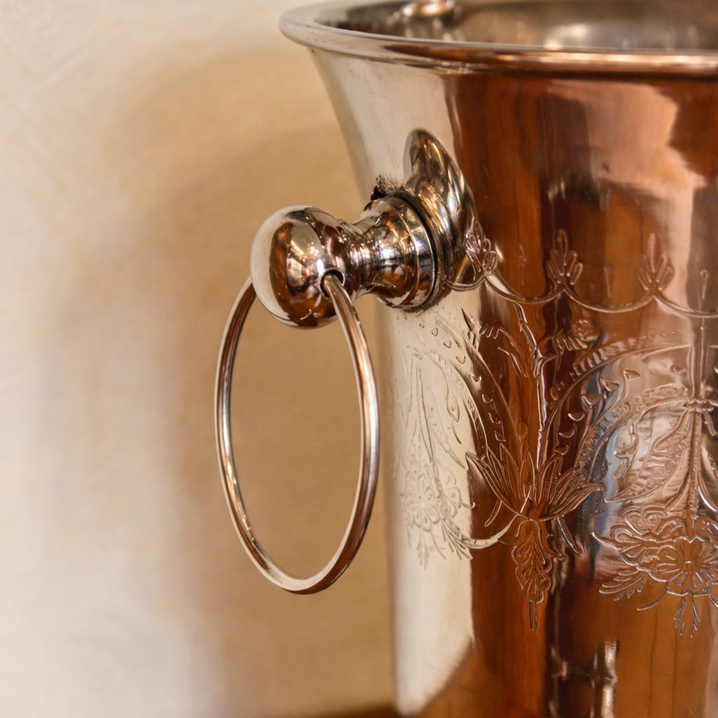 Close-up of an engraved silver champagne bucket handle with polished ring detail on a wooden table, highlighting intricate craftsmanship and reflective finish.