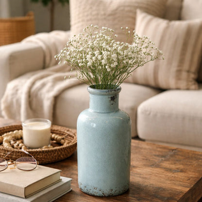 Light blue crackle-finish ceramic vase with white baby’s breath flowers styled on a wooden coffee table in a cozy living room setting.