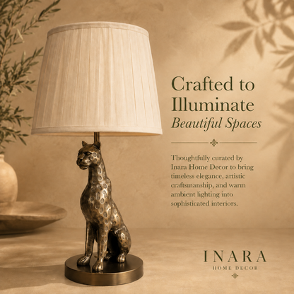 Luxury leopard table lamp with a pleated fabric lampshade in an antique brass finish, showcased on a warm beige editorial background with elegant typography by Inara Home Decor.