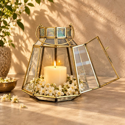 Elegant handcrafted brass and clear glass lantern featuring a lit pillar candle surrounded by fresh white mogra flowers, creating a warm festive home décor display.