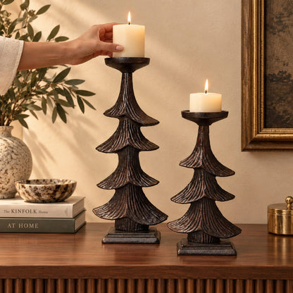 Decorative metal Christmas tree candle holder set with lit pillar candles being placed on a luxury console table.