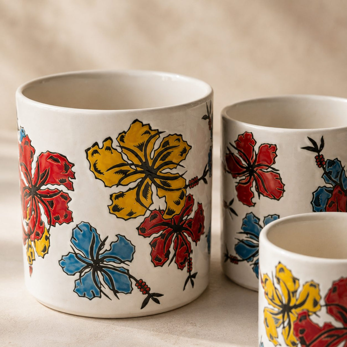 Close-up of a hand-painted floral ceramic planter set of 3 featuring vibrant red, yellow, and blue hibiscus artwork on premium white ceramic decorative indoor plant pots.