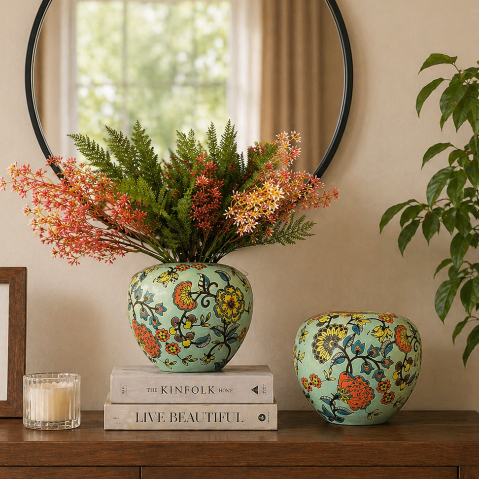 Front view of floral ceramic vases styled on a wooden console table with decorative books, candle, framed art, and greenery in a warm modern interior.