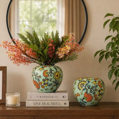 Front view of floral ceramic vases styled on a wooden console table with decorative books, candle, framed art, and greenery in a warm modern interior.