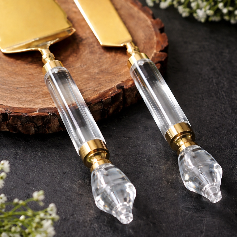 Close-up of gold cake server and knife set with clear acrylic handles on a dark stone surface