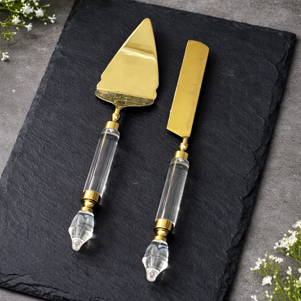 Gold cake server and knife set with clear acrylic handles displayed on a black slate board