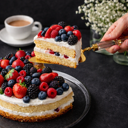 Gold cake server with acrylic handle lifting a slice of berry layer cake from a dessert stand