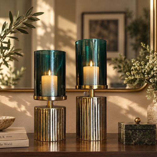 Green glass hurricane candle holder set styled with lit cream pillar candles on a luxury wooden console table.