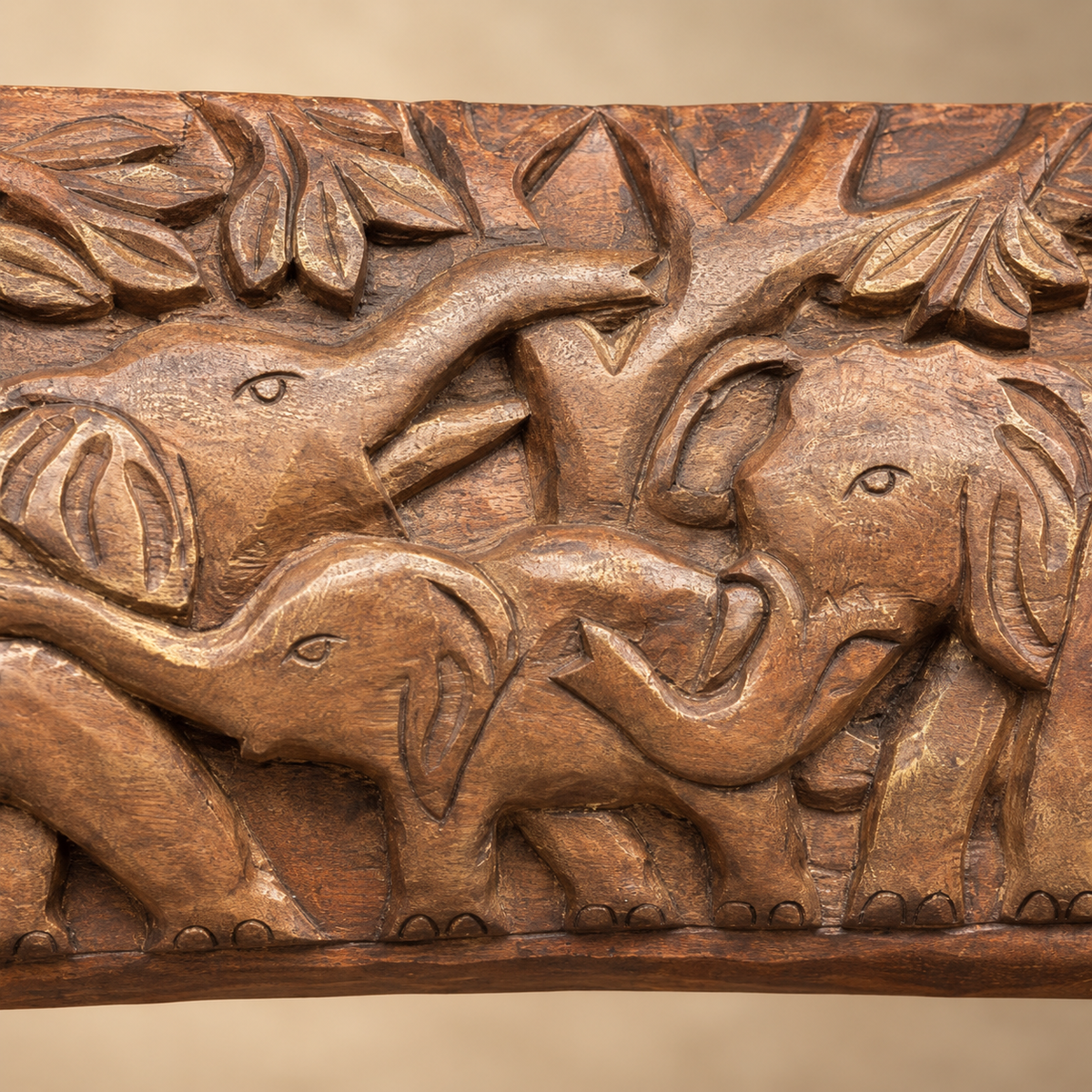 Close-up of hand-carved wooden elephant family showing detailed elephants, leaves and artisanal wood carving.