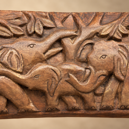 Close-up of hand-carved wooden elephant family showing detailed elephants, leaves and artisanal wood carving.