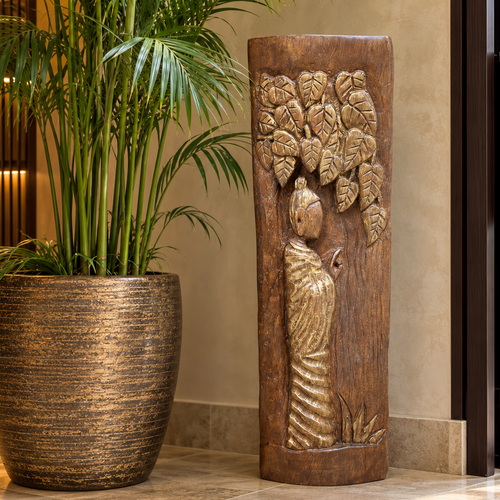 Hand-carved wooden decorative sculpture with antique gold detailing styled beside a tall palm plant at an elegant home entrance.