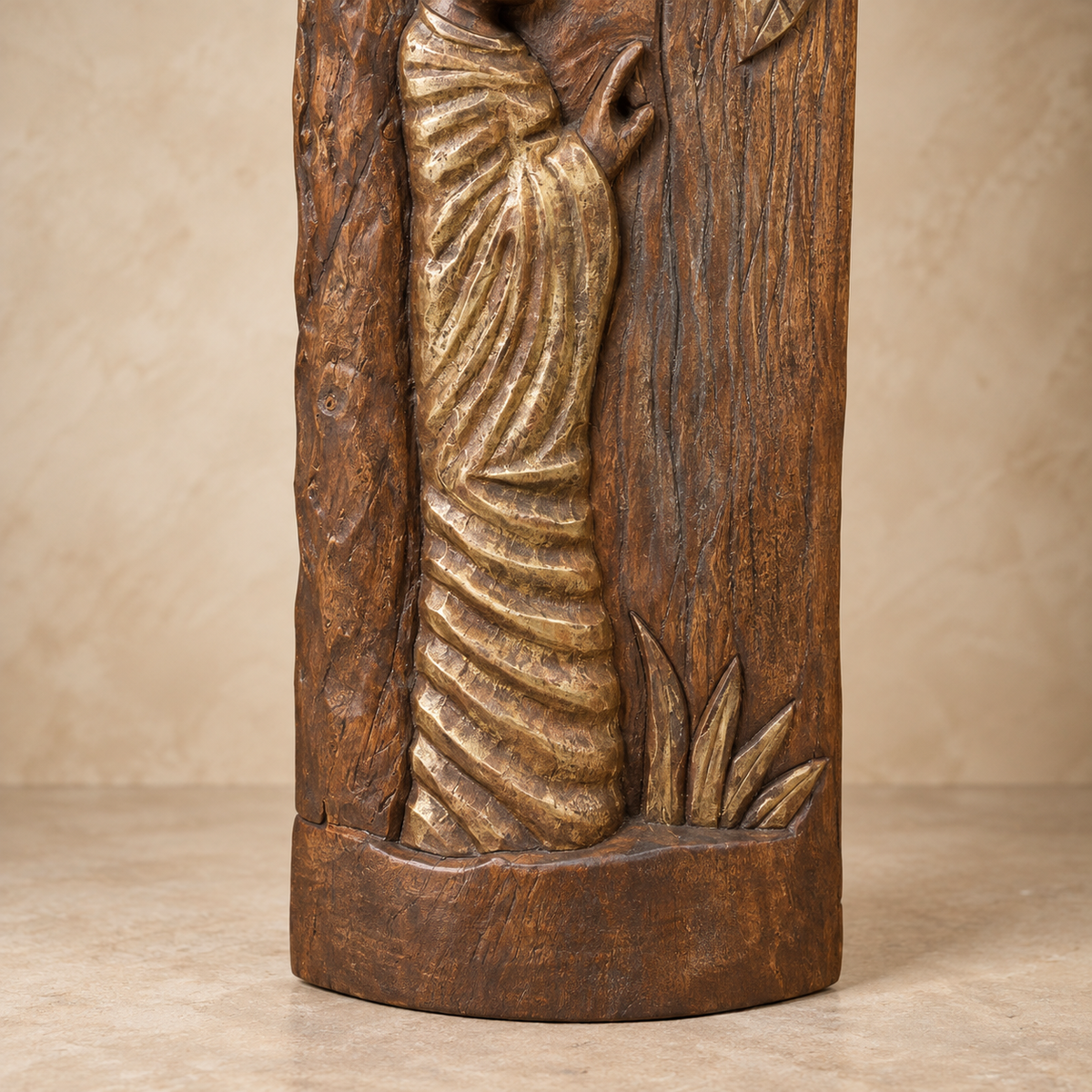 Close-up of hand-carved wooden sculpture showing antique gold-toned robe detailing, carved foliage and natural wood base.