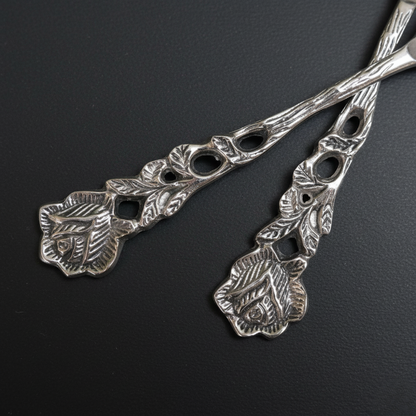 A high-resolution close-up of two silver spoons crossed over each other, highlighting the detailed embossed rose and leaf pattern on the vintage-style handles.