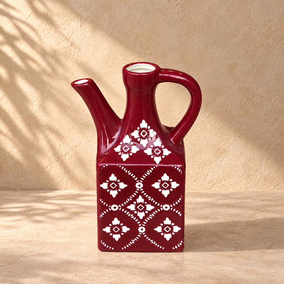 Hand-painted burgundy ceramic decorative vase jug with white floral motif displayed against a warm beige textured backdrop in luxury editorial home décor styling.