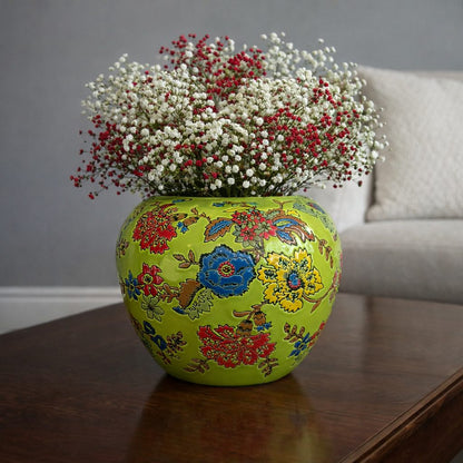 Hand-painted green floral ceramic vase with white and red baby’s breath flowers placed on a dark polished wood coffee table against a grey wall.