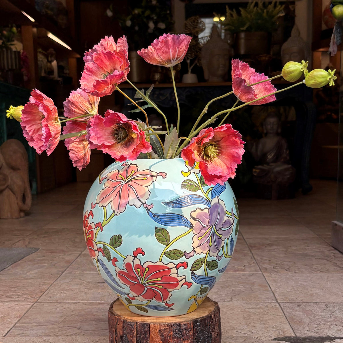 Close-up of a handcrafted ceramic jar with intricate floral artwork and red poppy flowers in an elegant indoor setting.