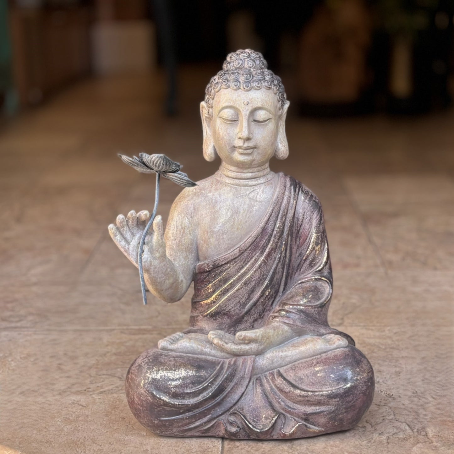 Close-up of a handcrafted Buddha statue in a meditative pose, showing detailed textures, gold-toned highlights on the robe, and a metallic lotus stem.