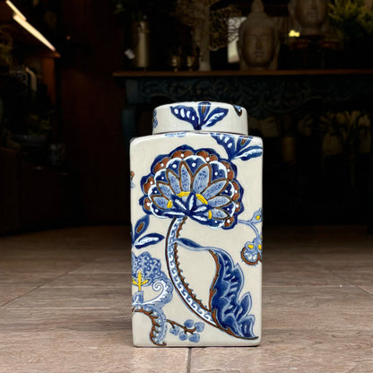 Front view of a handcrafted rectangular ceramic ikat jar with a matching lid, showcasing detailed blue floral and vine patterns against a cream base, captured in a professional showroom setting.
