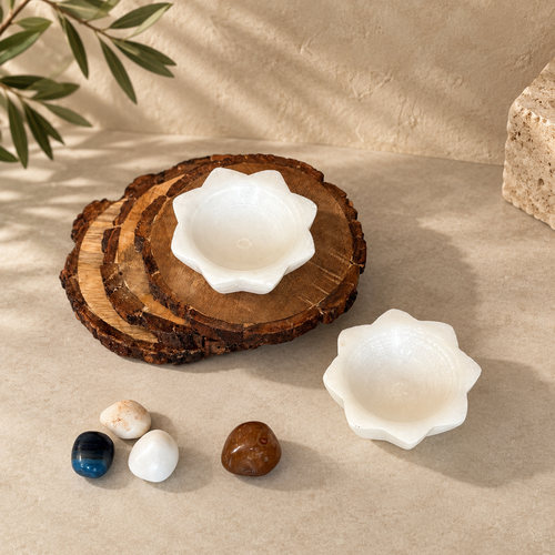 Top view of handcrafted white selenite lotus tea light holder set with natural wooden coasters and decorative crystals on a luxury beige background.