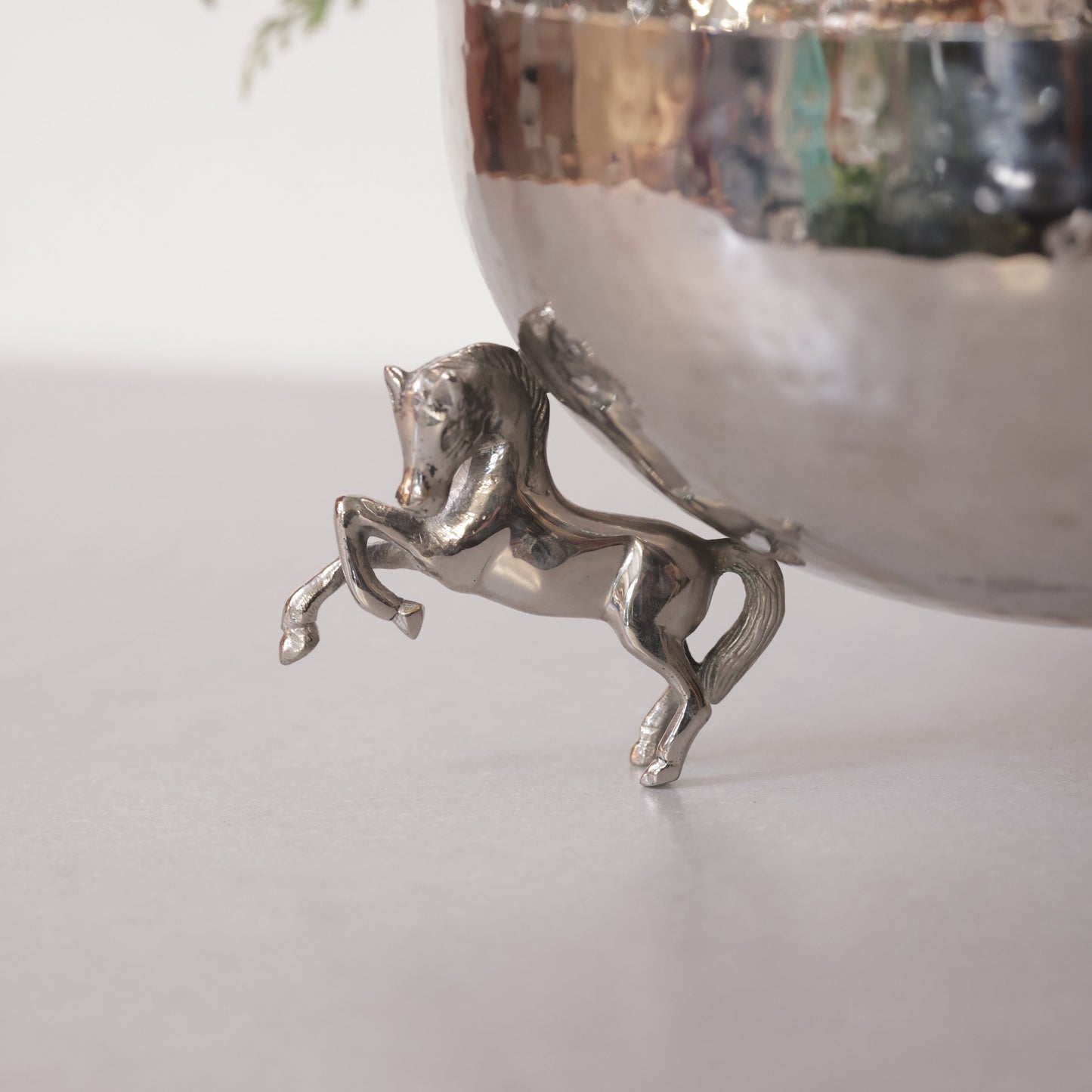 close-up shot of a polished silver horse figurine acting as a decorative leg for a hammered metal bowl.