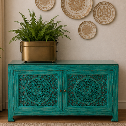 Handcrafted turquoise wooden console with intricate carved doors styled with a vintage brass planter and lush fern in a luxury living room featuring decorative wall plates