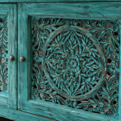 Close-up detailing of intricate hand-carved floral cut work on a distressed turquoise wooden cabinet door, highlighting fine craftsmanship and textured finish.