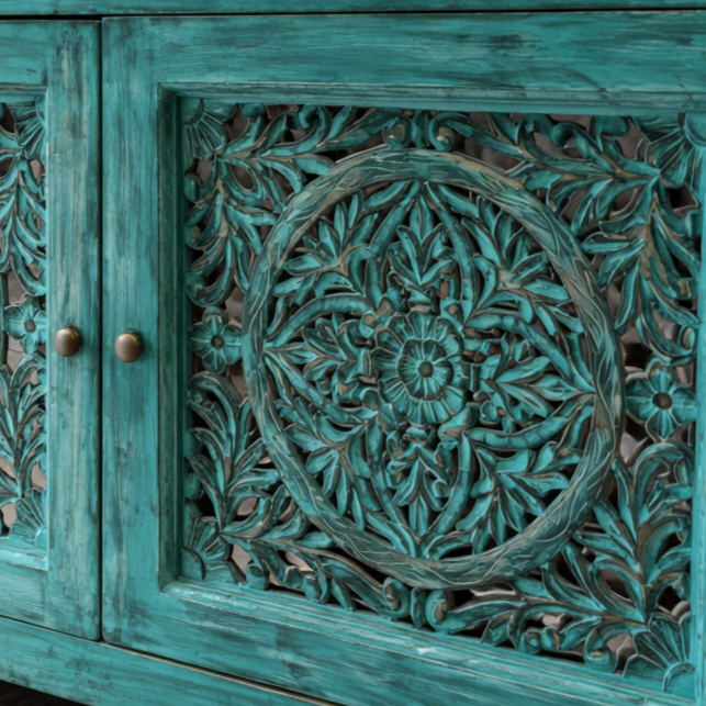 Close-up detailing of intricate hand-carved floral cut work on a distressed turquoise wooden cabinet door, highlighting fine craftsmanship and textured finish.