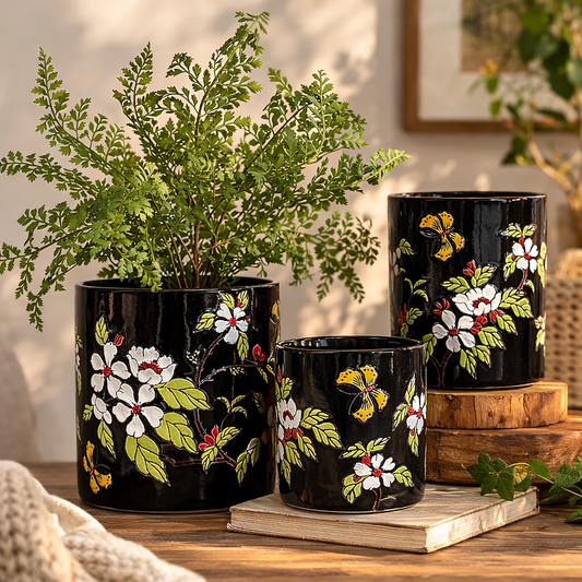 Hand-painted black ceramic floral planter set with green indoor plants displayed on a wooden tabletop in a modern home decor setting
