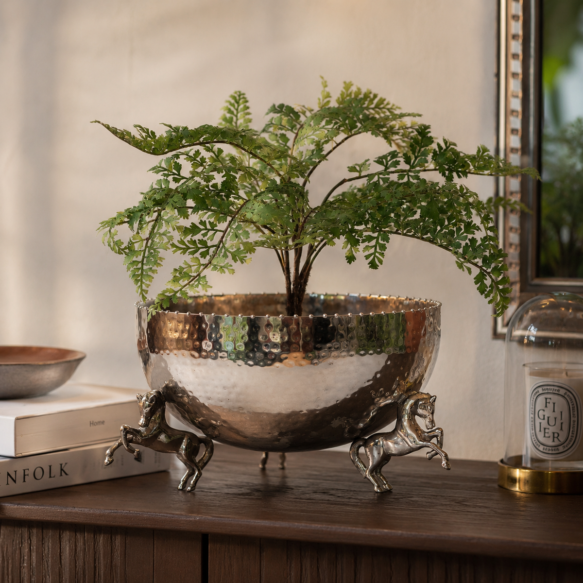Luxury hammered stainless steel decorative bowl with sculptural horse legs used as a stylish planter, displayed with lush green foliage on a wooden console table for elegant home décor.