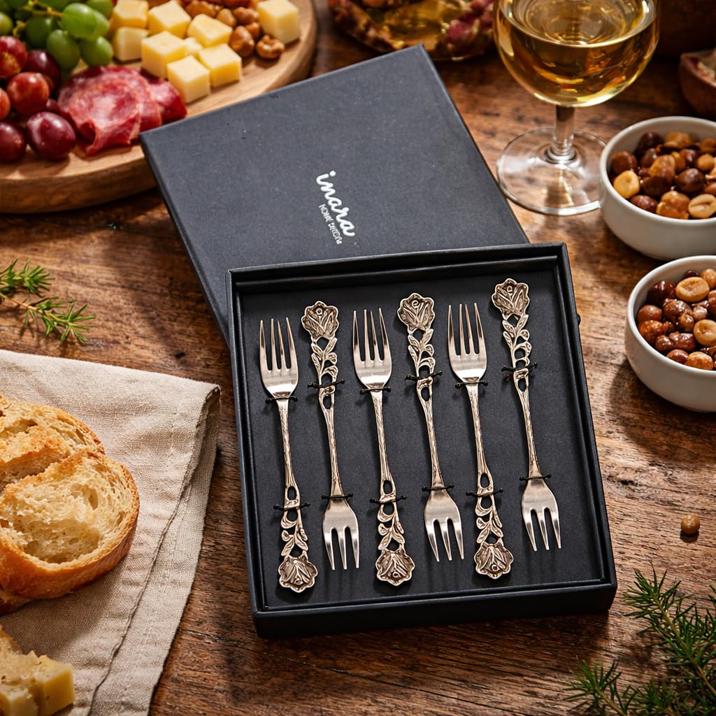 Luxury silver rose-patterned dessert forks presented in a premium black "Inara Home Decor" branded gift box on a rustic wooden table with a charcuterie board.