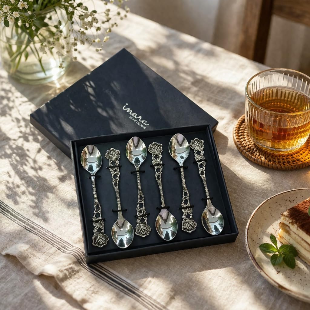 A premium black "Inara Home Decor" gift box containing a set of six silver rose-themed dessert spoons, presented on a linen tablecloth in soft natural lighting.