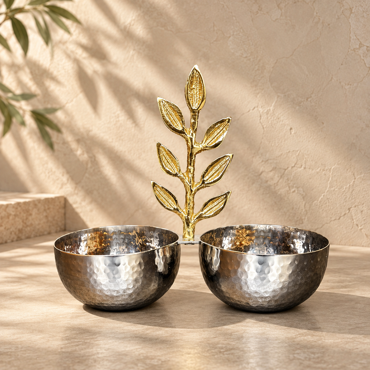 Inara luxury silver hammered stainless steel double bowl with an ornate brass golden leaf motif handle set against a warm neutral studio backdrop.