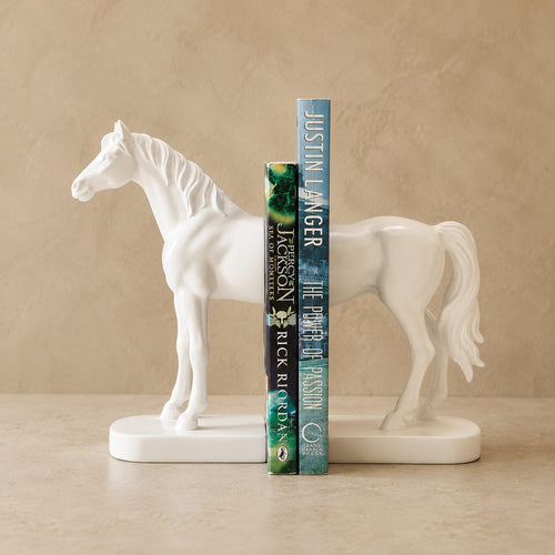 White resin horse bookends holding hardcover books on a premium beige studio backdrop, luxury decorative book ends for bookshelves, home office, and living room décor.