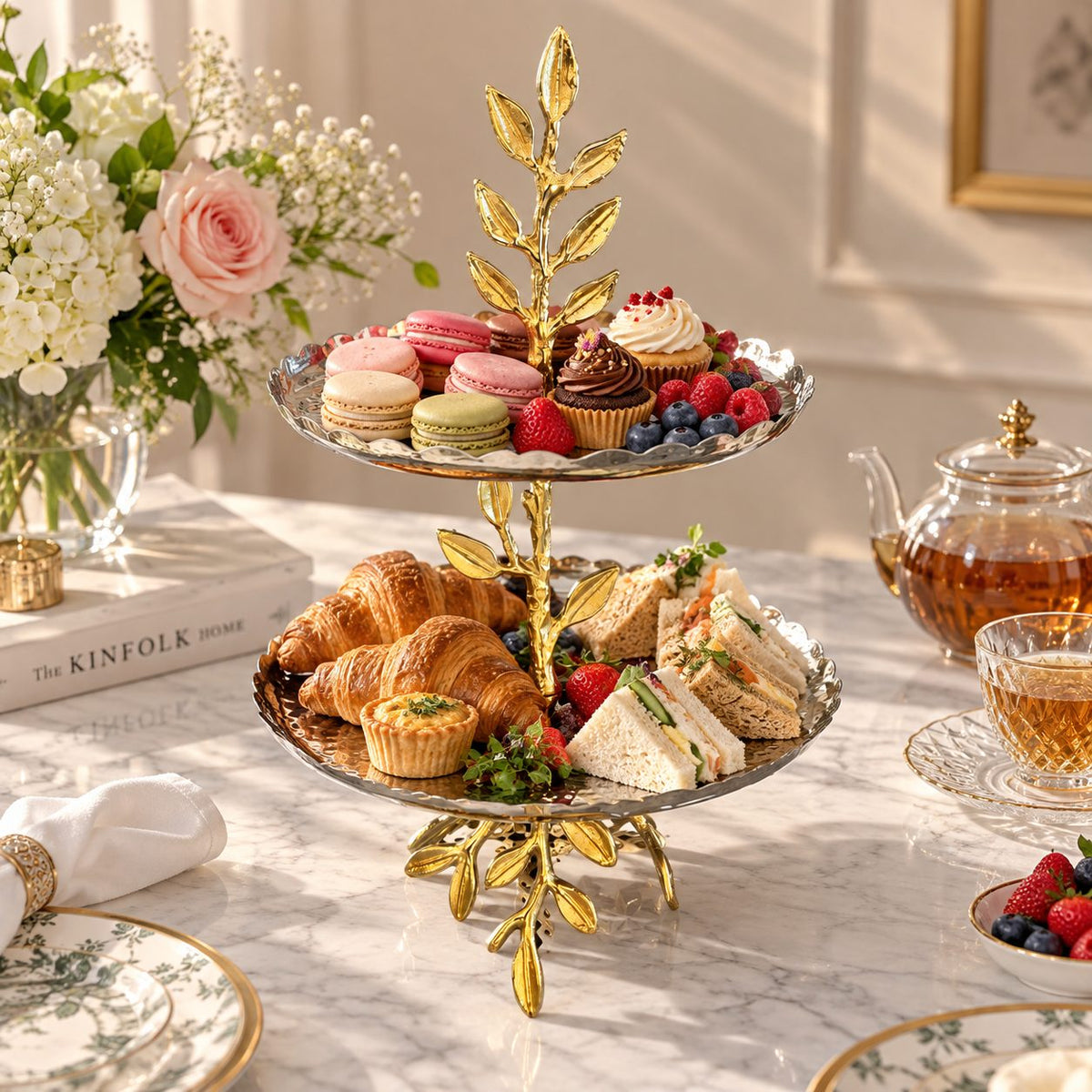 Elegant two tier leaf serving stand styled with macarons, cupcakes, sandwiches, croissants and fresh berries for a luxury afternoon tea table setting.