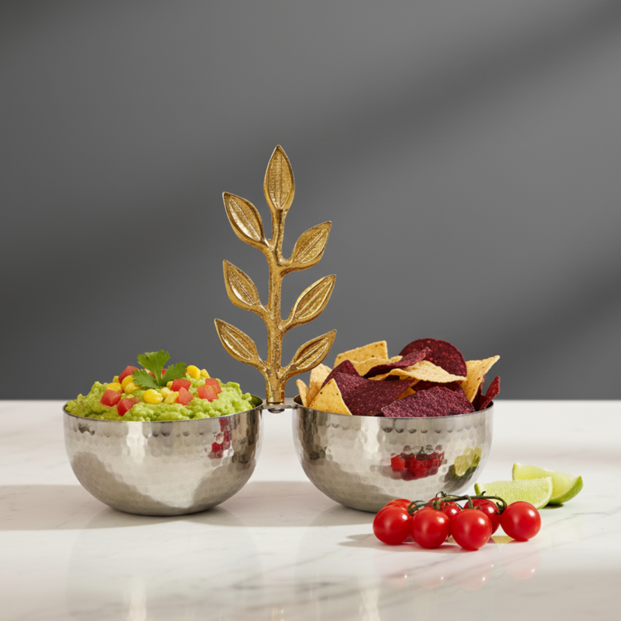 Hammered stainless steel double snack serving bowl with gold leaf handle, filled with guacamole and tortilla chips on a modern tabletop.